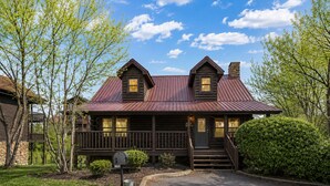A log cabin with a porch, a chimney, and a well-maintained lawn. - Cozy 4BR Cabin 3 miles from Dollywood, Hot Tub, Game Room, Fast Wifi (Sevierville)