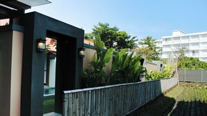 Ein modernes Gebäude mit dunkler Fassade, einem Bambuszaun und einem Gartenbereich mit jungen Pflanzen.