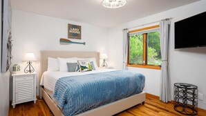 A bedroom with a bed, bedside tables, a TV, a window with curtains, and a wall sign. - All Sports Long Lake/Hot Tub/Private Beach/Dock/Kayaks/Gameroom/Pets OK (Traverse City)