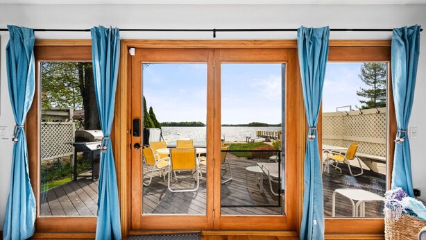 A room with a sliding glass door leading to an outdoor deck with yellow chairs and a grill. - All Sports Long Lake/Hot Tub/Private Beach/Dock/Kayaks/Gameroom/Pets OK (Traverse City)