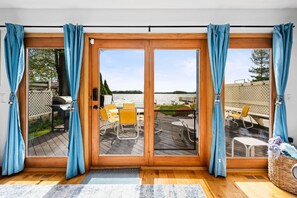A room with a sliding glass door leading to an outdoor deck with yellow chairs and a grill. - All Sports Long Lake/Hot Tub/Private Beach/Dock/Kayaks/Gameroom/Pets OK (Traverse City)