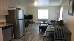 A compact kitchen with a refrigerator, a dishwasher, and a dining area with a table and chairs. - Elite 2-bedroom apartment in Moose Creek with WiFi (North Pole)
