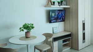 A modern living room with a round white table, two beige chairs, a TV mounted on the wall, a wooden cabinet, and a potted plant. - The Catalina Suite at The Beacon Makati (Makati)