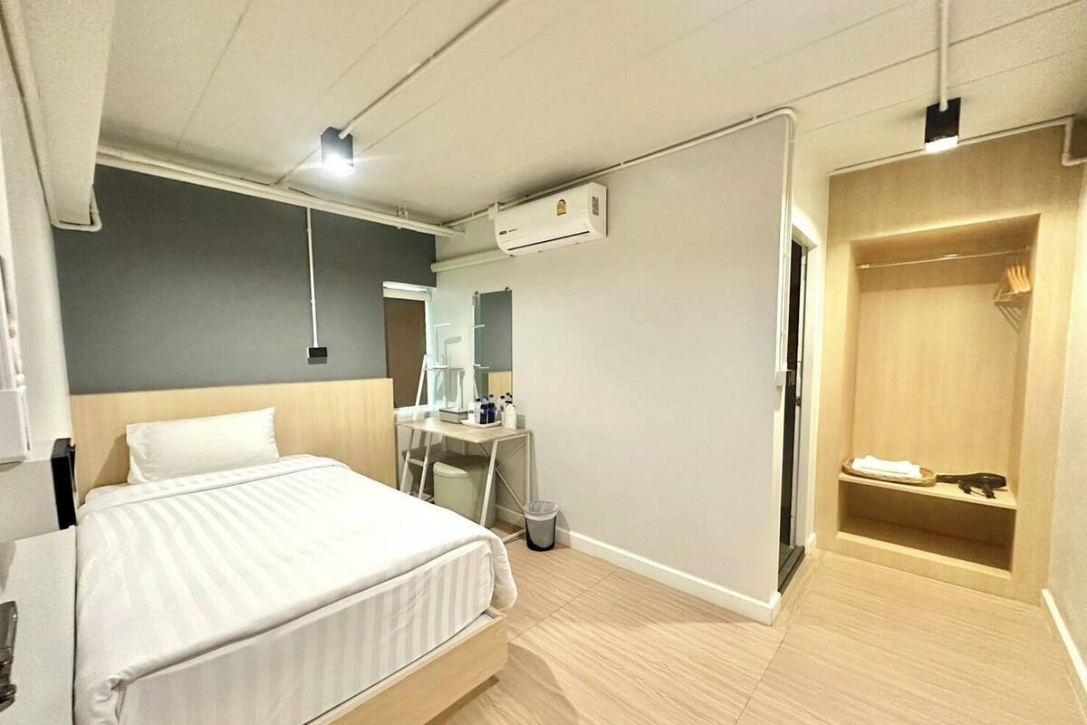 A modern hotel room with a bed, a desk with a mirror, an air conditioning unit, and a walk-in closet.