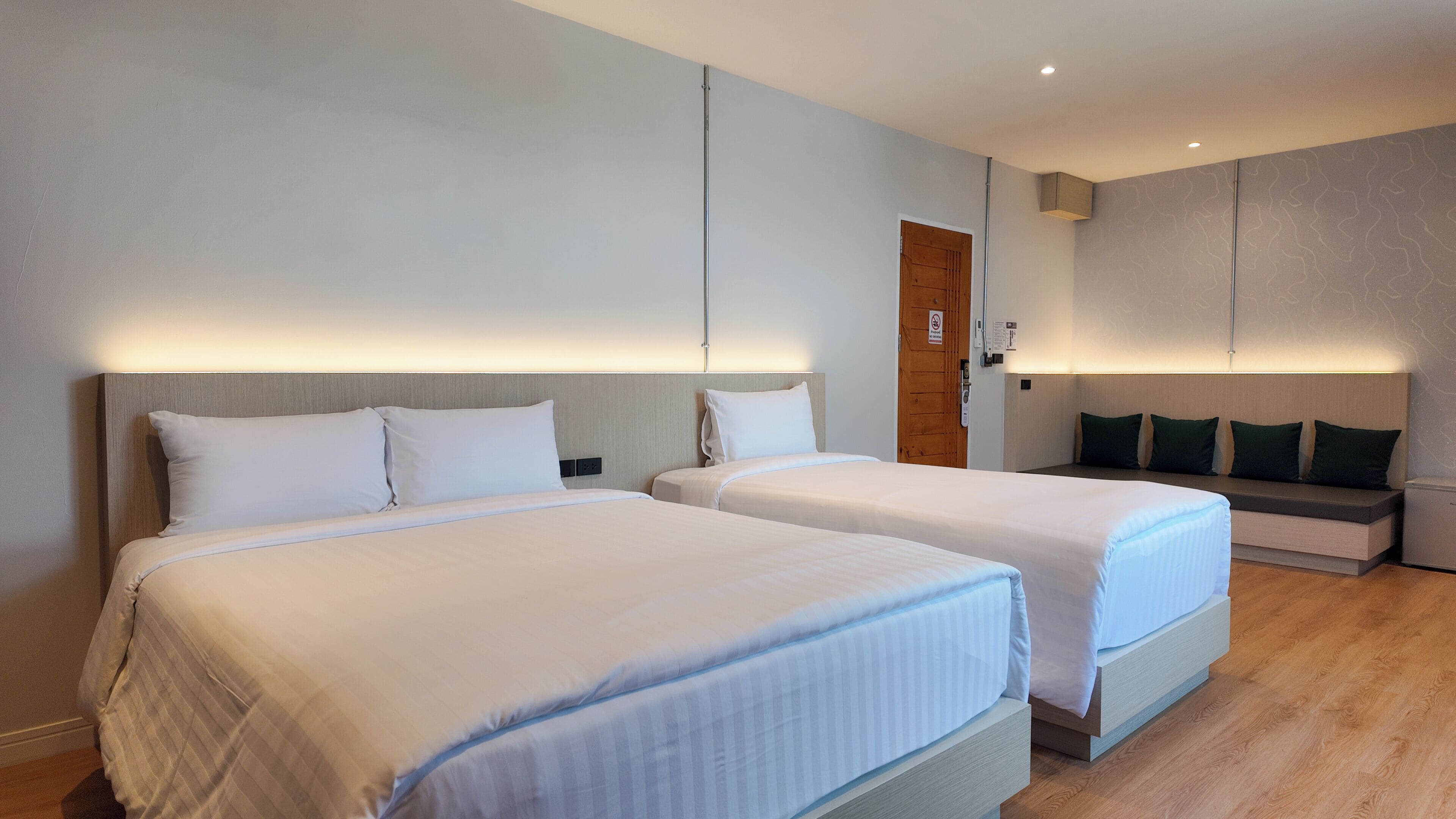 Une chambre d’hôtel avec deux lits, une porte en bois et un banc avec des coussins.