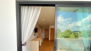 Una habitación moderna con piso de madera, un escritorio pequeño y vista a un paisaje exuberante a través de un ventanal.
