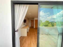 Una habitación moderna con piso de madera, un escritorio pequeño y vista a un paisaje exuberante a través de un ventanal.