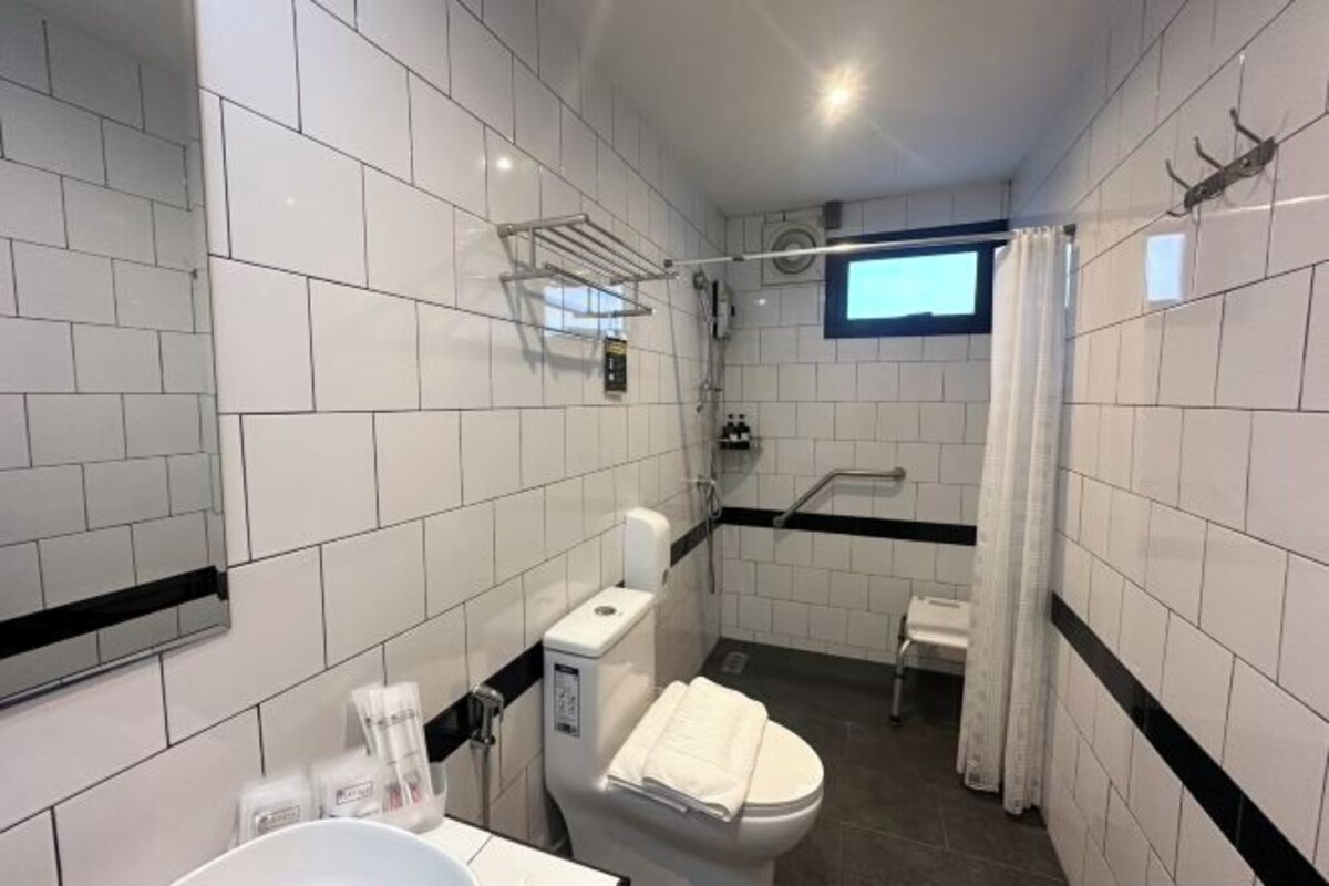 A modern bathroom with white tiles, a toilet, a sink, a shower, and a window.