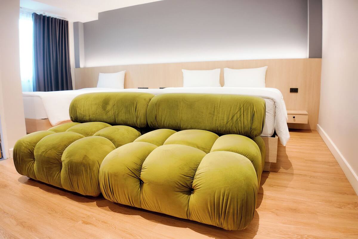 A modern hotel room with a large bed, a green tufted sofa, and a wooden floor.
