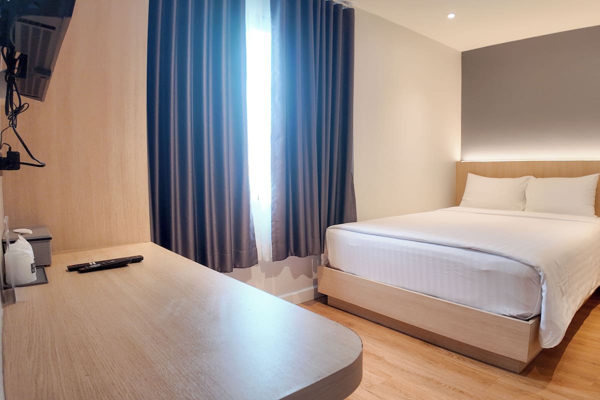 A modern hotel room with a neatly made bed, a wooden desk, and a large window with curtains.