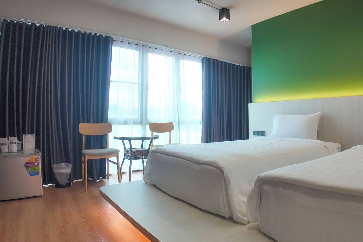 A hotel room with two beds, a small table, chairs, a desk with a computer, and a window with curtains.