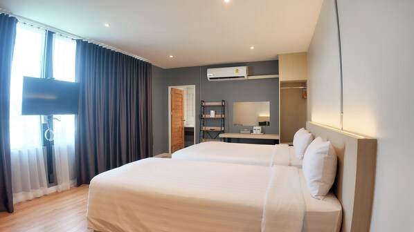 A hotel room with two beds, a desk, a mirror, and an air conditioning unit.