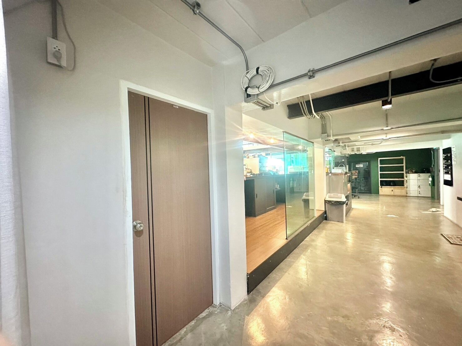 A spacious, well-lit hallway with a wooden door, a glass partition, and a clean, polished concrete floor.