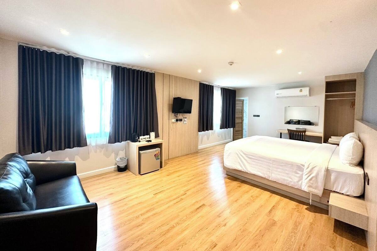 A modern hotel room with a large bed, a sofa, a desk, and a TV.