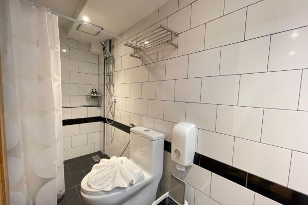 A modern bathroom with white tiles, a black and white tiled shower area, a white toilet, and a soap dispenser.