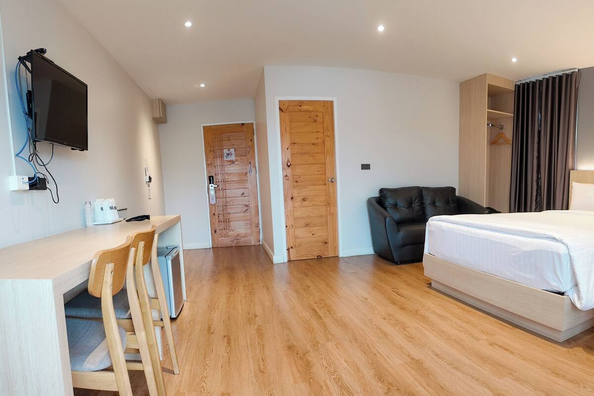 A hotel room with two beds, a desk with a chair, a TV mounted on the wall, and a wooden door.