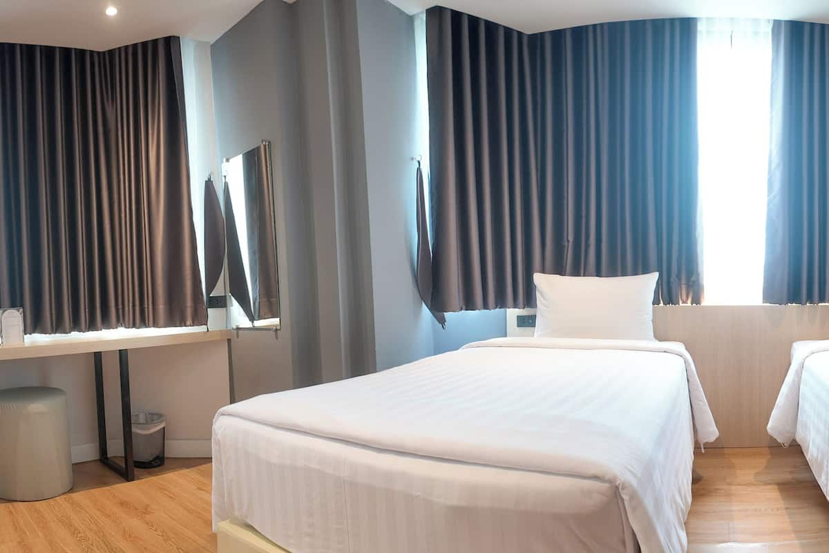 A hotel room with two beds, a desk, a mirror, and an air conditioning unit.