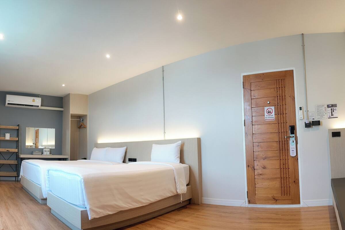 A modern hotel room with a large bed, a separate sofa, a wooden door, and a bathroom with a shower and sink.