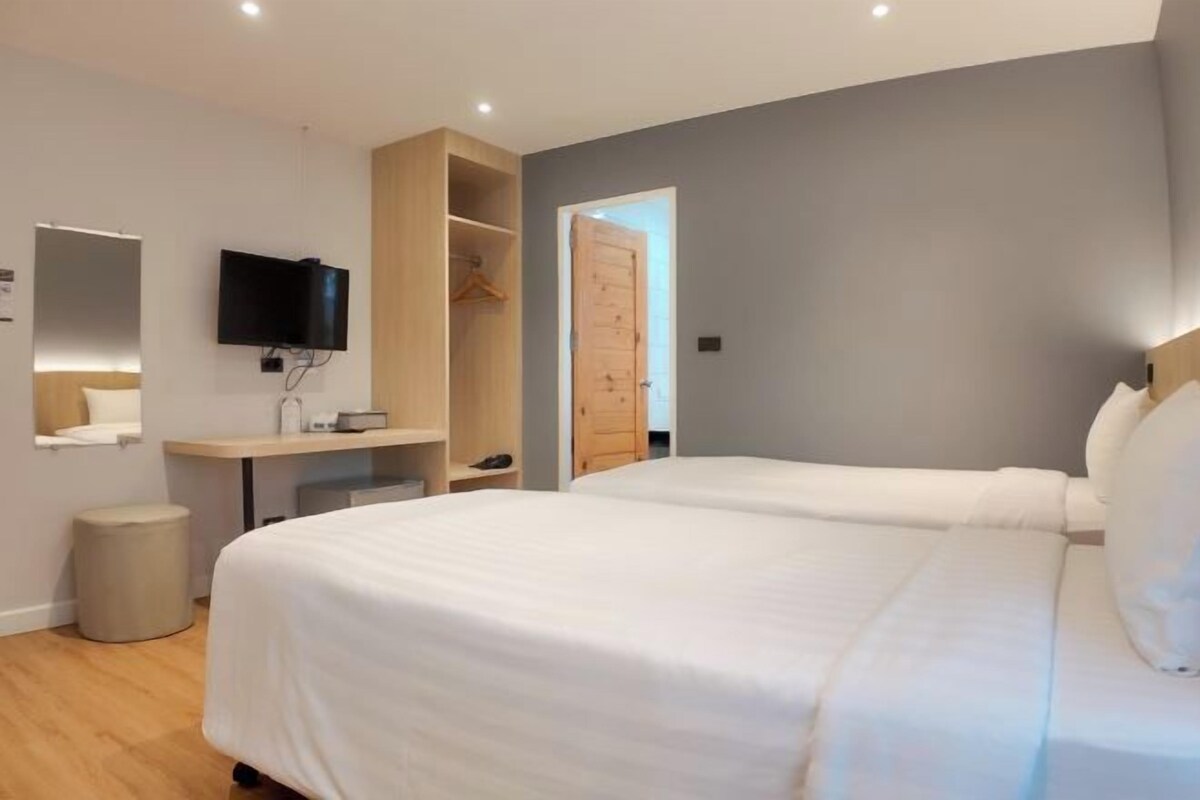 A modern hotel room with two beds, a desk, a TV, and a wardrobe.