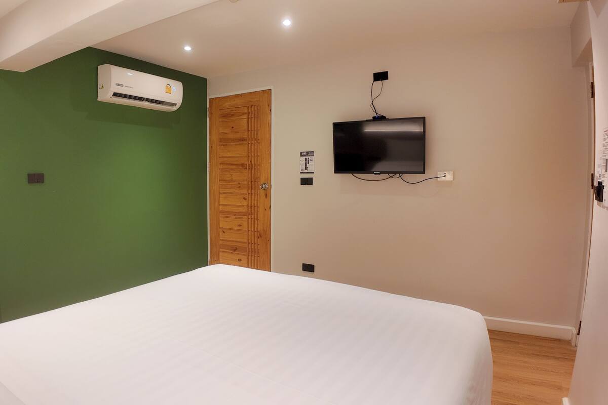 A bedroom with a bed, an air conditioner, a wooden door, and a mounted TV.