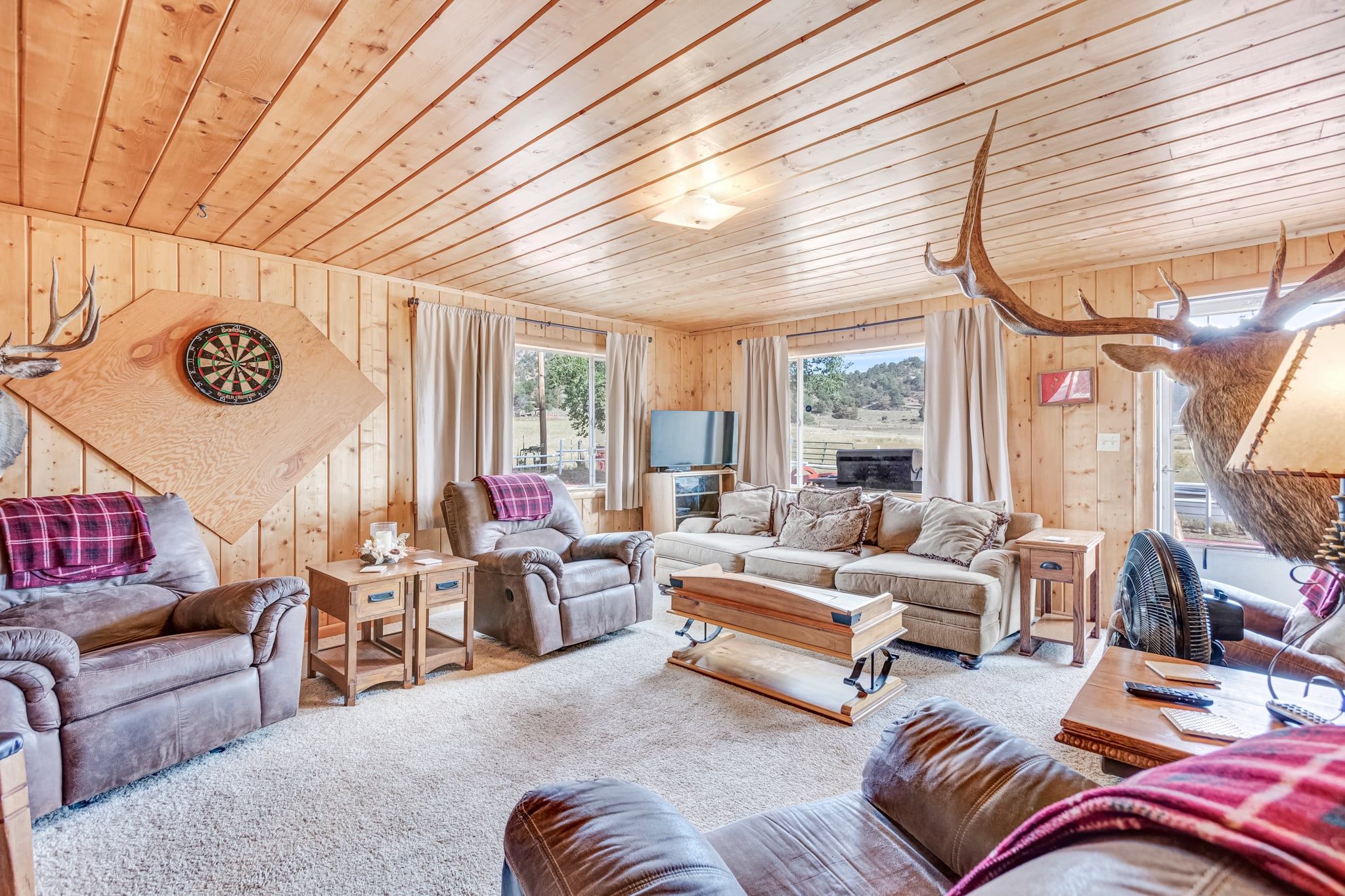 L’intérieur chaleureux d’un chalet avec des murs en bois, un canapé en cuir, une table basse et une tête de cerf accrochée au mur.