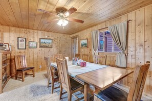 A wooden interior with a dining table, chairs, a ceiling fan, and framed pictures on the walls.