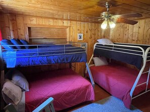A room with two bunk beds, wooden walls, a ceiling fan, and a small framed picture on the wall.