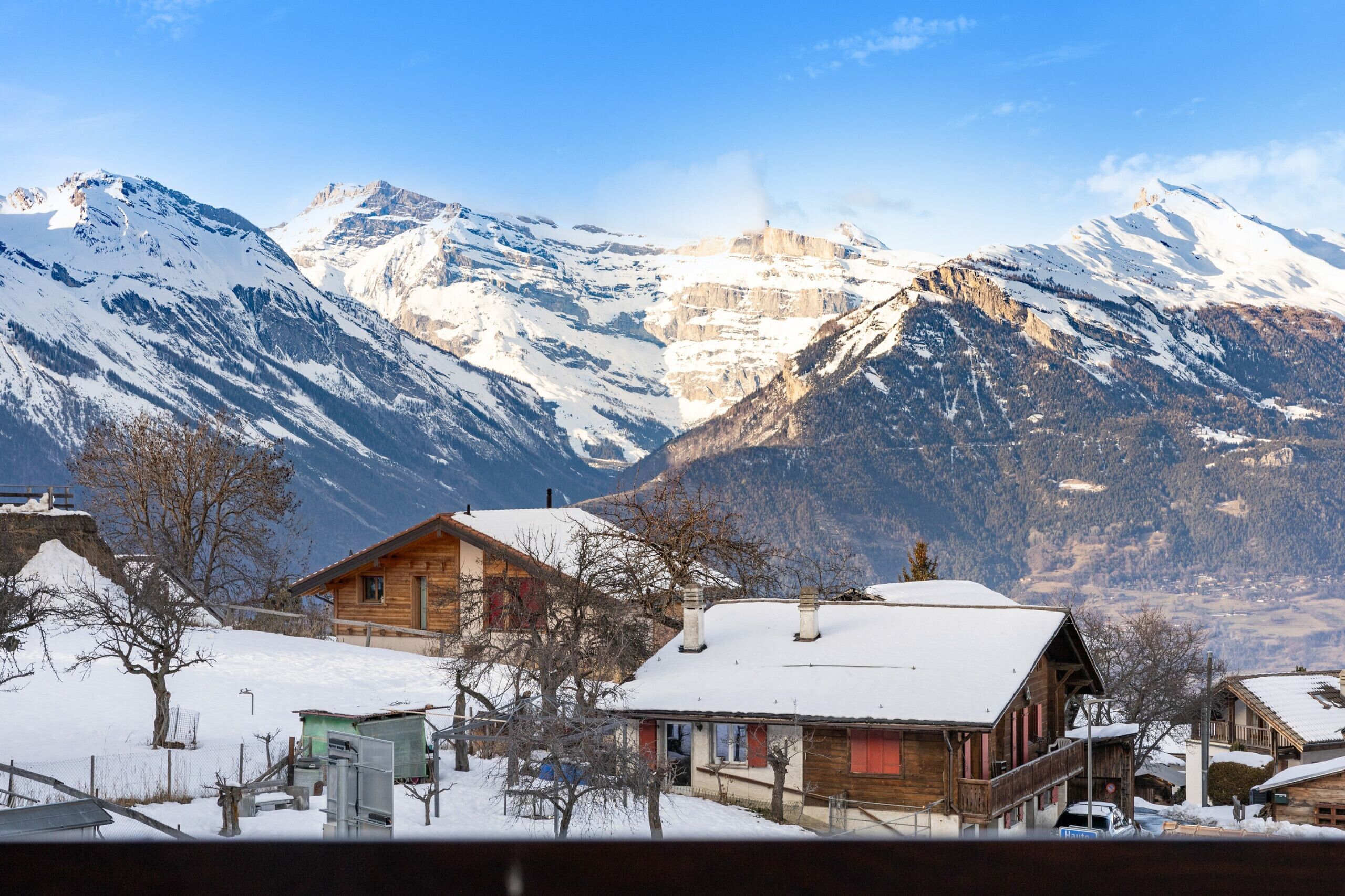 Eine Holzhütte mit schneebedecktem Dach, umgeben von Bergen und wolkenlosem Himmel.