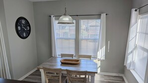 Un coin repas avec une table en bois, deux chaises, une horloge et une suspension.