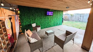 Un espace extérieur aménagé en terrasse, avec des meubles en osier, un mur végétal et un écran de télévision.