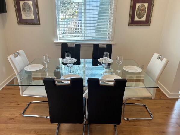 A dining area with a glass table, black chairs, and framed pictures on the walls.