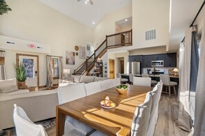 A spacious living area with a wooden dining table, a sofa, and a staircase leading to an upper level.