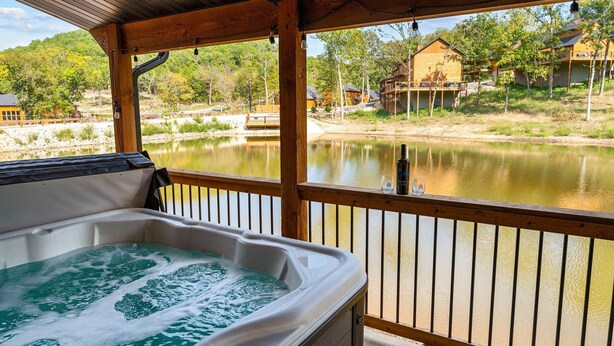 Un jacuzzi en una terraza de madera con vistas a un lago tranquilo y casas al fondo.