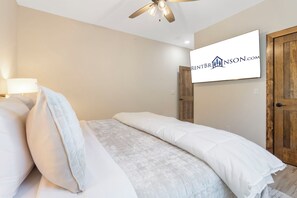 A bedroom with a bed, a ceiling fan, a wall-mounted TV, and a wooden door.