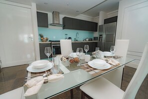 Un comedor moderno con una mesa de vidrio dispuesta para cuatro personas, rodeada de sillas blancas.
