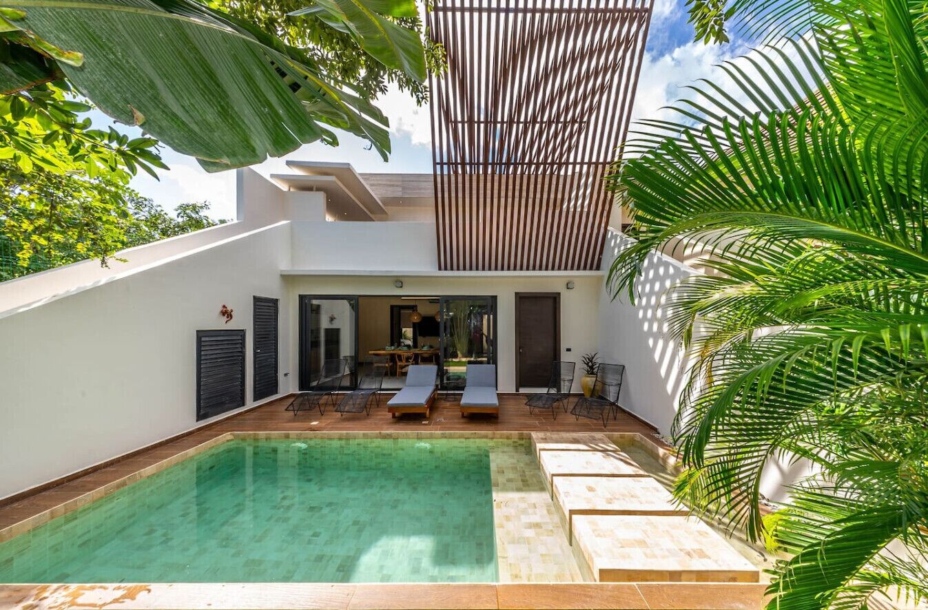 A modern pool area with a clear pool, lounge chairs, and a covered seating area.