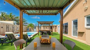 En udendørs patio med et bord dækket til to, en pool og et overdækket siddeområde.