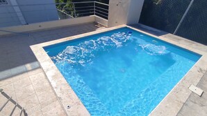 A rectangular swimming pool with clear blue water, surrounded by a tiled deck. - Charming 3-bedroom apartment with WiFi, AC and a picuzzy in Santo Domingo Oeste. (Santo Domingo Oeste)