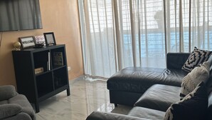 A modern living room with a black leather sofa, a grey armchair, a black entertainment unit, and a ceiling fan. - Charming 3-bedroom apartment with WiFi, AC and a picuzzy in Santo Domingo Oeste. (Santo Domingo Oeste)