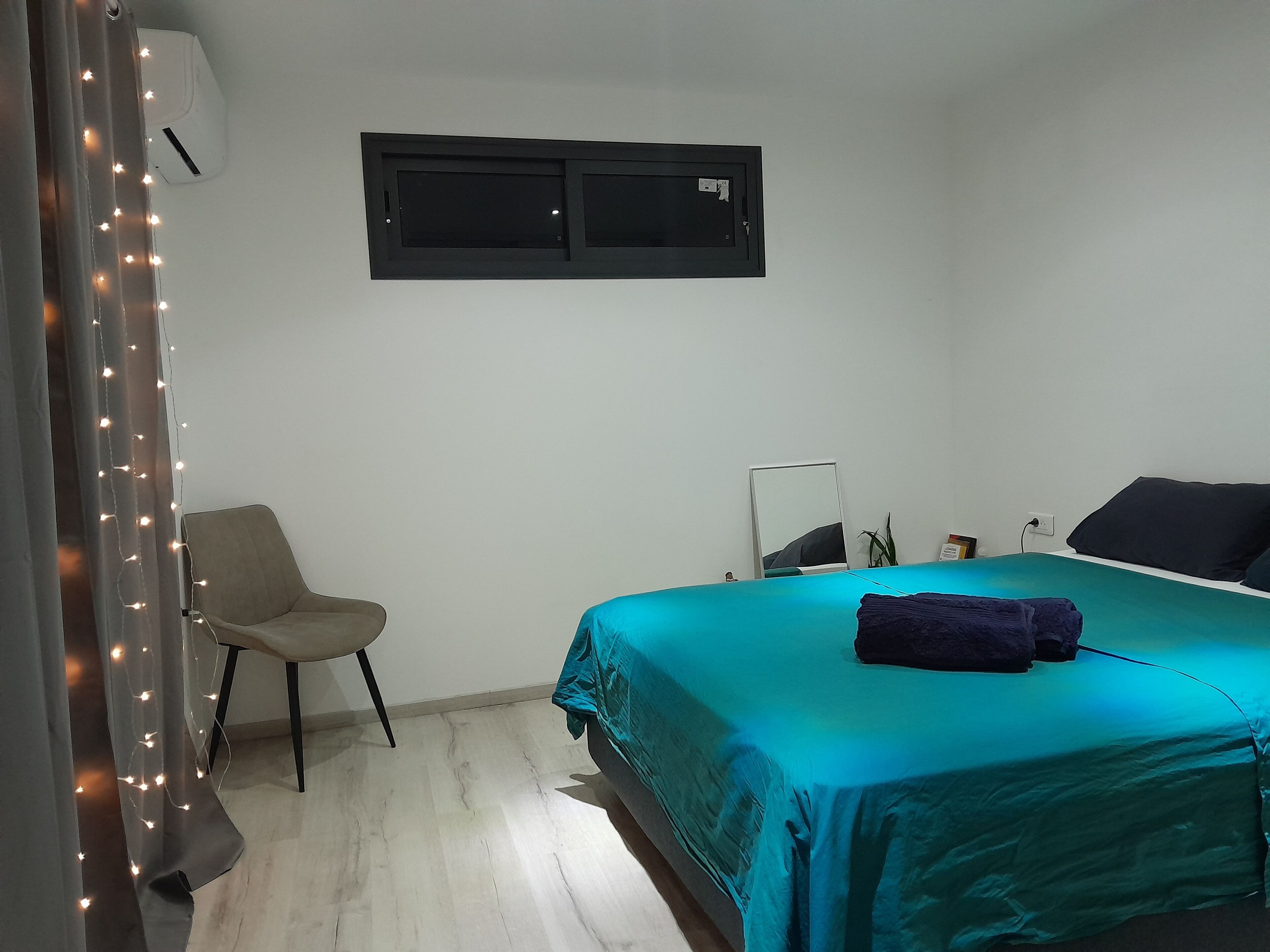 A bedroom with a bed, a chair, a mirror, and an air conditioning unit.