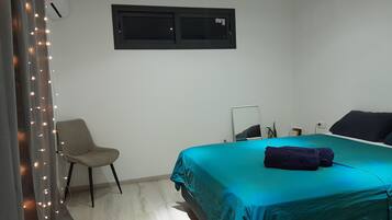 A bedroom with a bed, a chair, a mirror, and an air conditioning unit.
