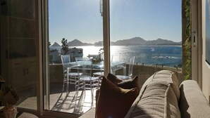 A balcony with a glass door, clear chairs, a table, and a sofa with a view of the sea and mountains. - Romantic Dream Arch View (Cabo San Lucas)