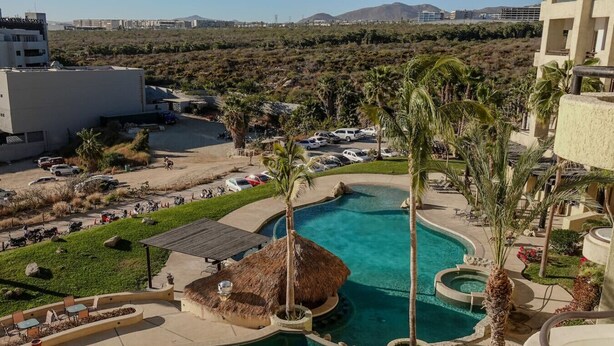 A resort with a large swimming pool, palm trees, and a view of the surrounding landscape. - Romantic Dream Arch View (Cabo San Lucas)