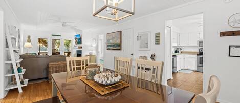 Un salón espacioso con una mesa de comedor de madera, paredes blancas y una cocina al fondo.