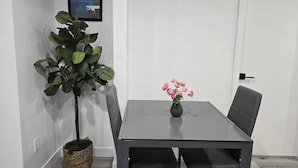 Un coin repas comprenant une table, des chaises, une plante en pot et un vase de fleurs.