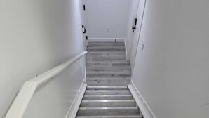 Un escalier étroit avec des marches en bois et des murs blancs, menant à une porte située en haut.