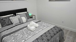 Une chambre moderne avec un grand lit, une literie à motifs, une table de chevet avec une lampe et un tableau sur le thème de la plage accroché au mur.