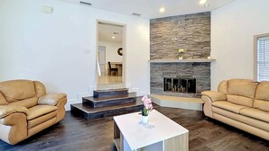 A living room with two leather sofas, a white coffee table with a flower, a stone fireplace, and a staircase leading to another room. - WhiteIris-5-Bedroom Home with Pool, Mini Golf, & Heated Jacuzzi in Boynton Beach (Boynton Beach)