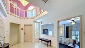 A spacious foyer with a staircase, a bench, a sofa, and a TV mounted on the wall. - WhiteIris-5-Bedroom Home with Pool, Mini Golf, & Heated Jacuzzi in Boynton Beach (Boynton Beach)