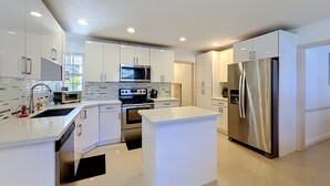 A modern kitchen with white cabinetry, stainless steel appliances, and a central island. - WhiteIris-5-Bedroom Home with Pool, Mini Golf, & Heated Jacuzzi in Boynton Beach (Boynton Beach)